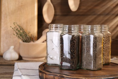 Photo of Different aromatic spices in glass jars on wooden table, closeup