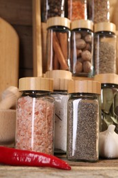 Photo of Different spices in glass jars and on wooden table, closeup