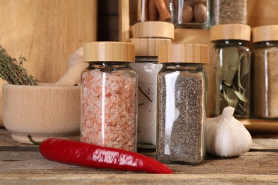 Photo of Different spices in glass jars and on wooden table, closeup