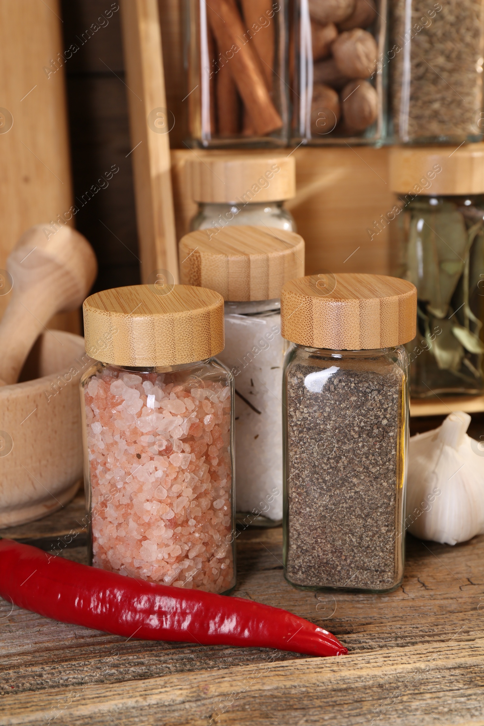 Photo of Different spices in glass jars and on wooden table, closeup