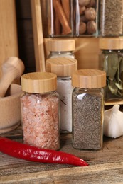 Photo of Different spices in glass jars and on wooden table, closeup