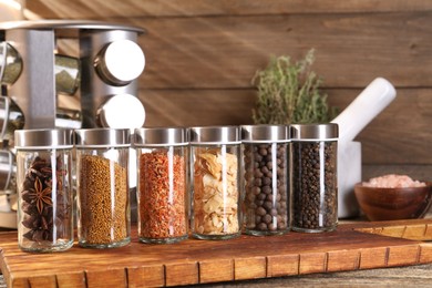Photo of Different spices in glass jars and on wooden table, closeup
