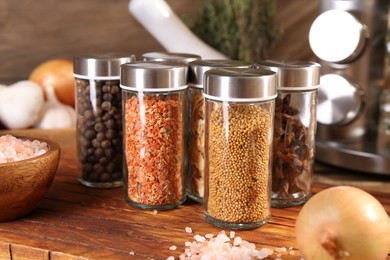 Photo of Different spices in glass jars and on wooden table, closeup