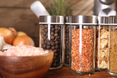 Photo of Different spices in glass jars and on wooden table, closeup