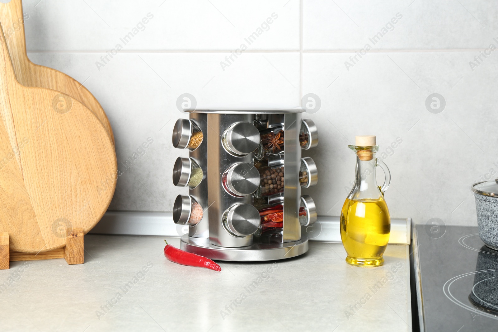 Photo of Set of different spices in glass jars and oil on light grey table in kitchen