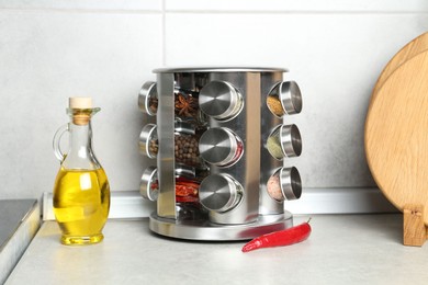 Photo of Set of different spices in glass jars and oil on light grey table in kitchen