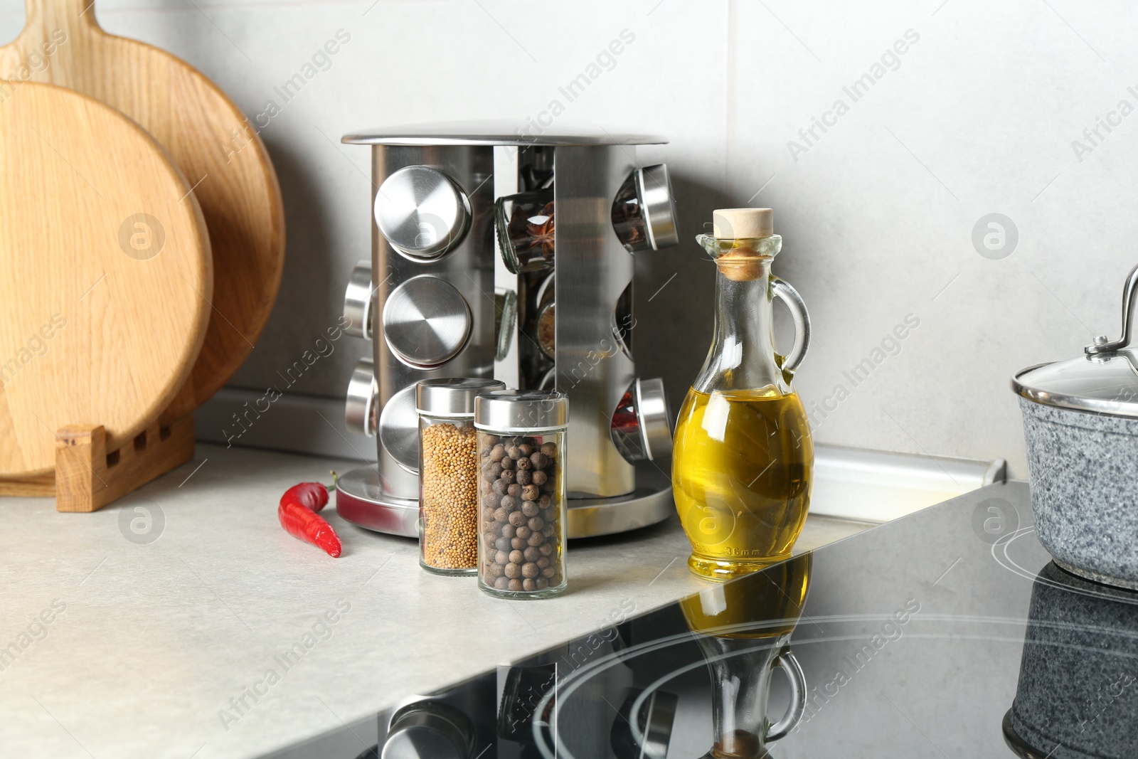 Photo of Set of different spices in glass jars and oil on light grey table in kitchen