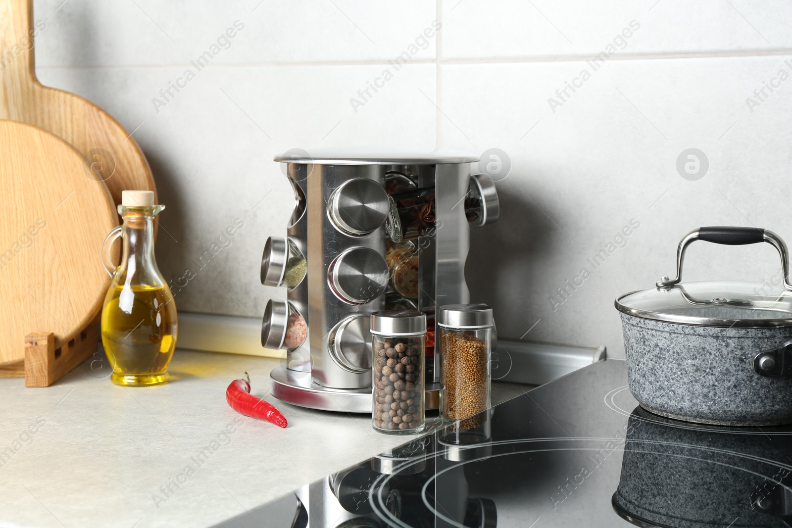 Photo of Set of different spices in glass jars and oil on light grey table in kitchen
