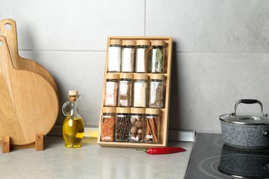Photo of Set of different spices in glass jars and oil on light grey table in kitchen