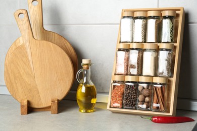 Photo of Set of different spices in glass jars and oil on light grey table in kitchen
