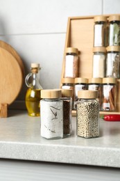 Photo of Different spices in glass jars on light grey table in kitchen