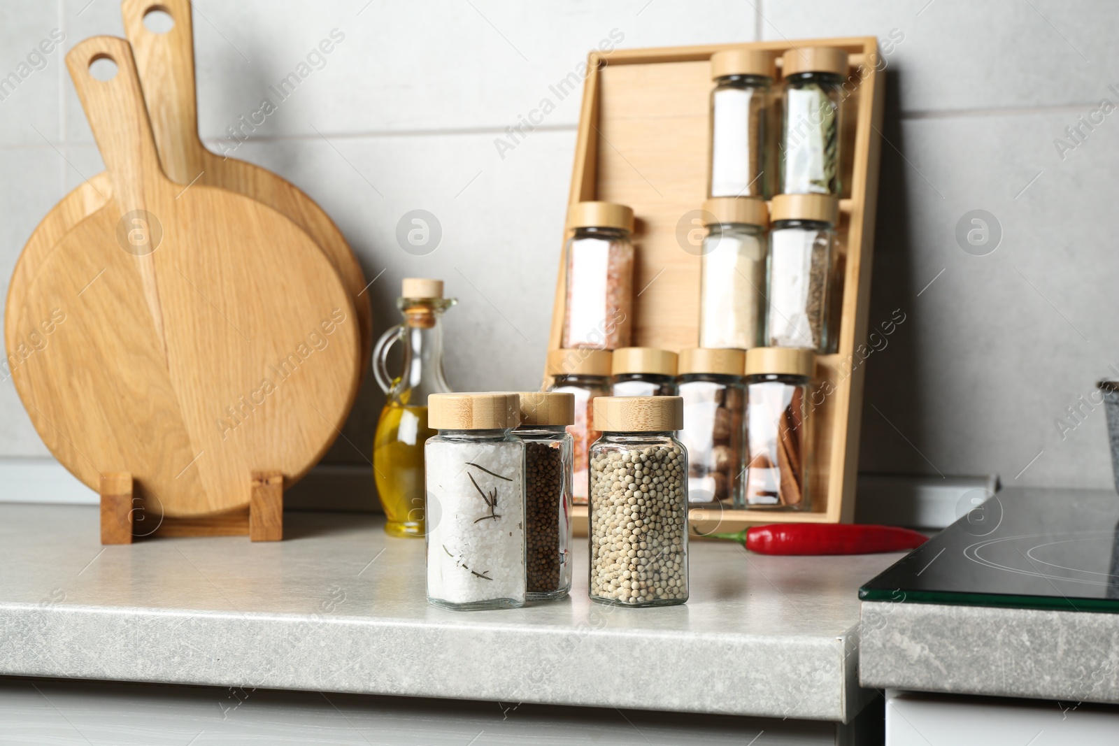 Photo of Different spices in glass jars on light grey table in kitchen