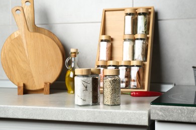 Photo of Different spices in glass jars on light grey table in kitchen