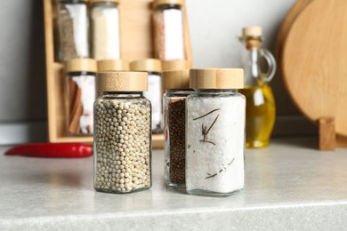 Photo of Different spices in glass jars on light grey table in kitchen, closeup