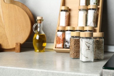 Photo of Different spices in glass jars and oil on light grey table in kitchen