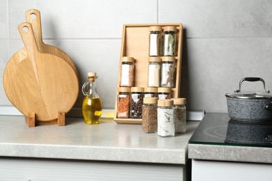 Photo of Set of different spices in glass jars and oil on light grey table in kitchen