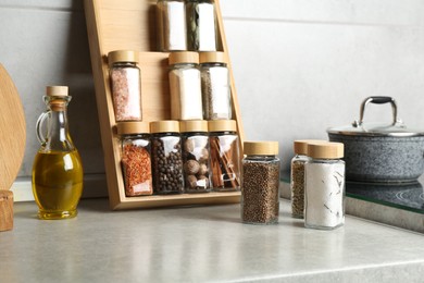 Photo of Set of different spices in glass jars and oil on light grey table in kitchen