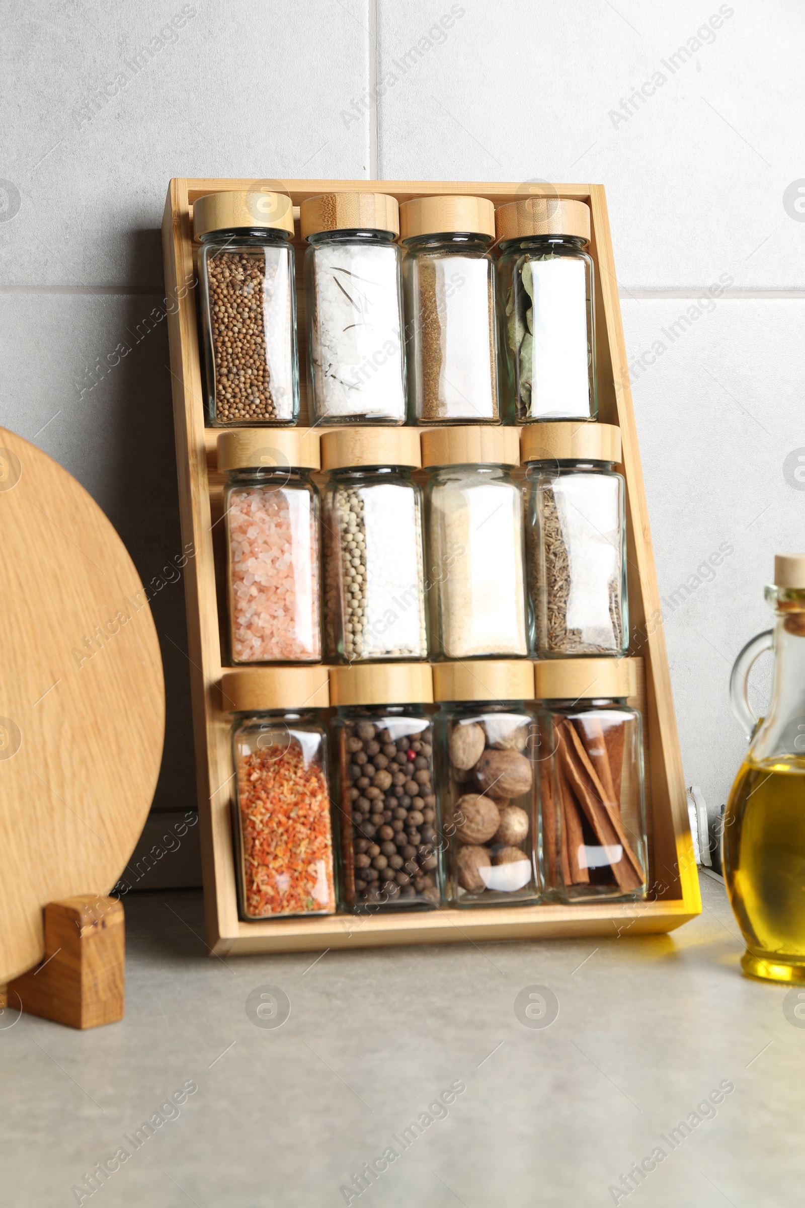 Photo of Set of different spices in glass jars and oil on light grey table in kitchen