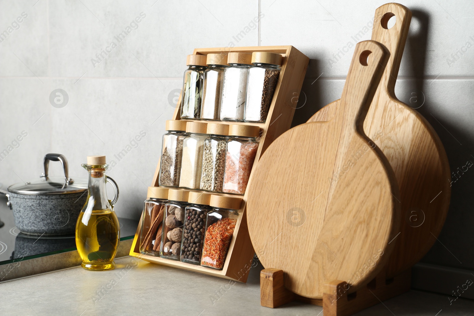 Photo of Set of different spices in glass jars and oil on light grey table in kitchen