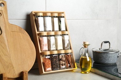 Photo of Set of different spices in glass jars and oil on light grey table in kitchen