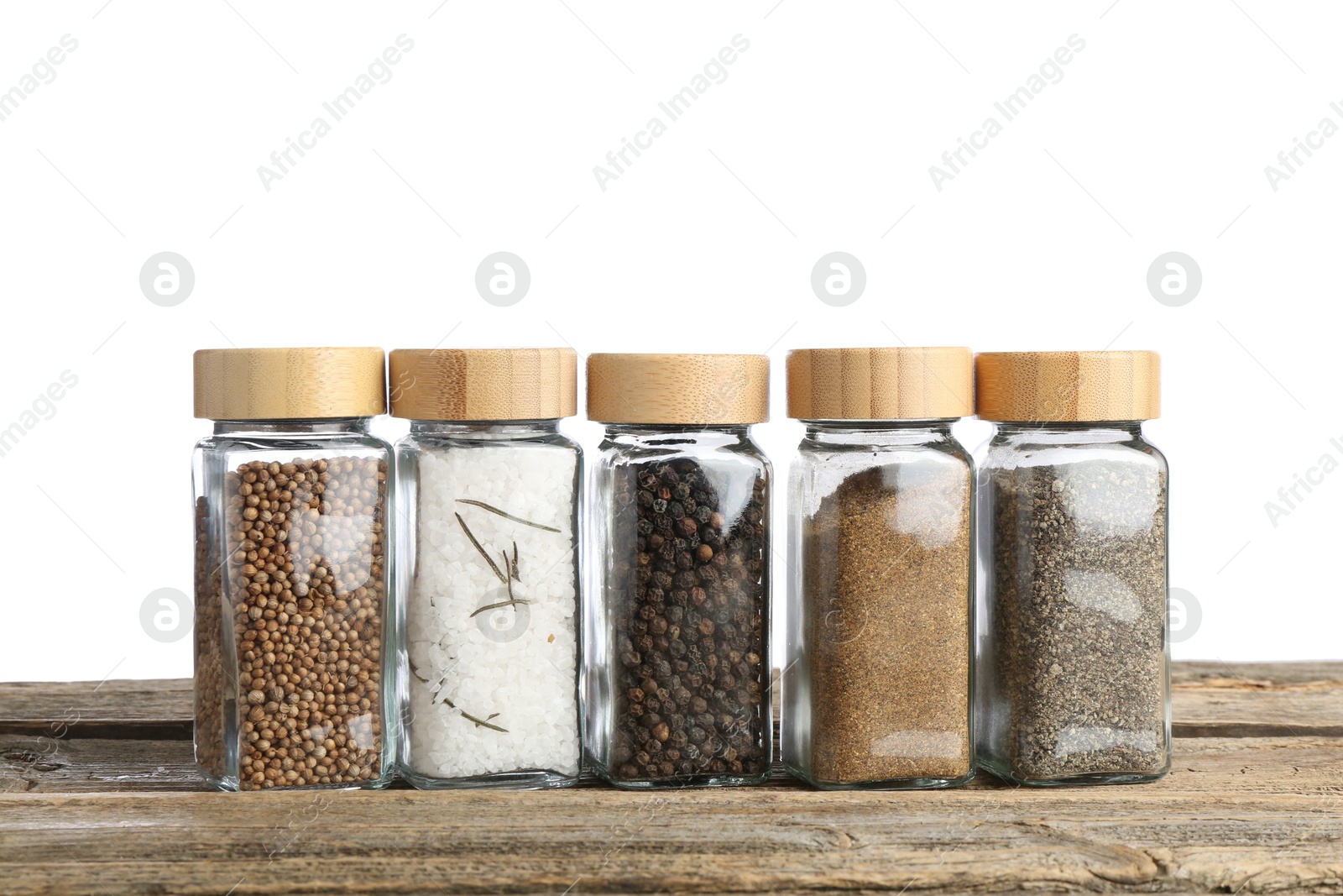 Photo of Many different aromatic spices in glass jars on wooden table against white background