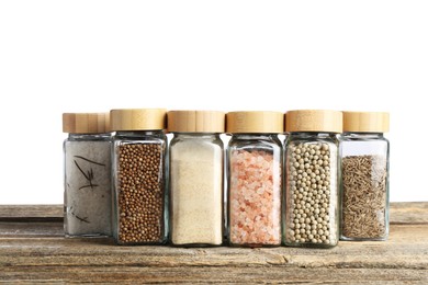 Photo of Many different aromatic spices in glass jars on wooden table against white background