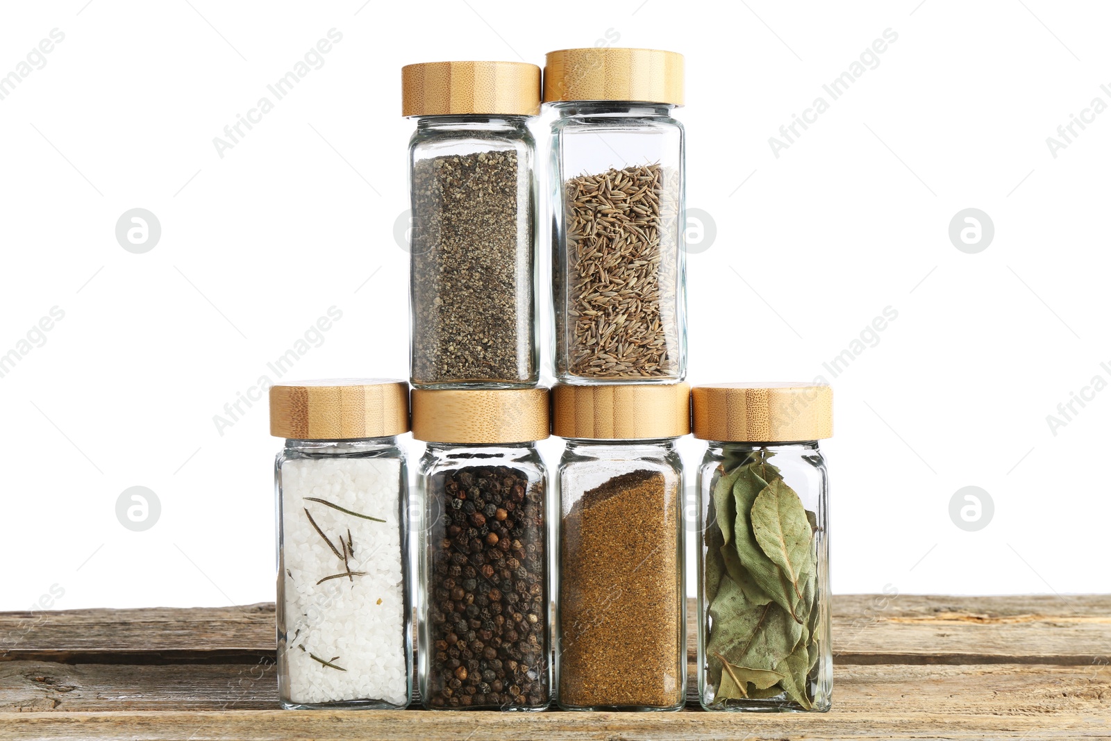 Photo of Many different aromatic spices in glass jars on wooden table against white background