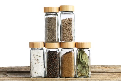 Photo of Many different aromatic spices in glass jars on wooden table against white background