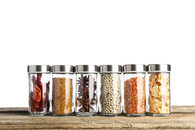 Photo of Many different aromatic spices in glass jars on wooden table against white background