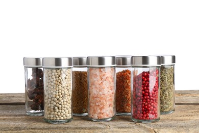 Photo of Many different aromatic spices in glass jars on wooden table against white background