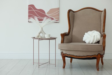Photo of Stylish armchair with cushion and other decor near white wall in room. Interior design