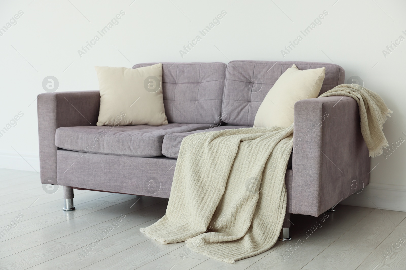 Photo of Comfortable gray sofa with blanket and cushions in room