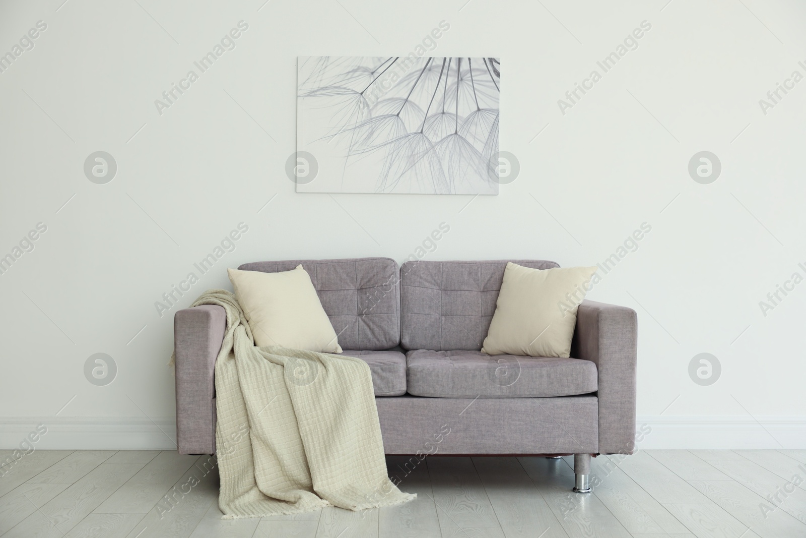 Photo of Comfortable gray sofa with blanket and cushions in room. Interior design