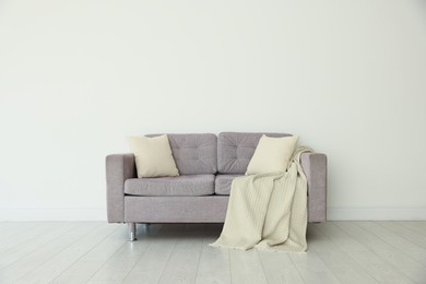 Photo of Comfortable gray sofa with blanket and cushions in room