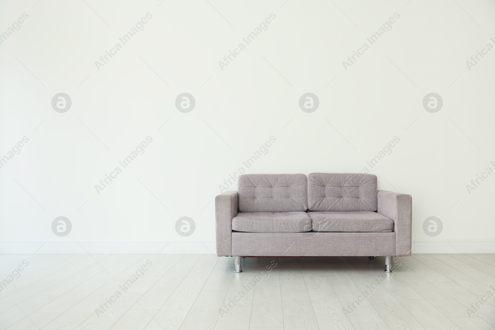 Photo of Comfortable gray sofa near white wall in room, space for text