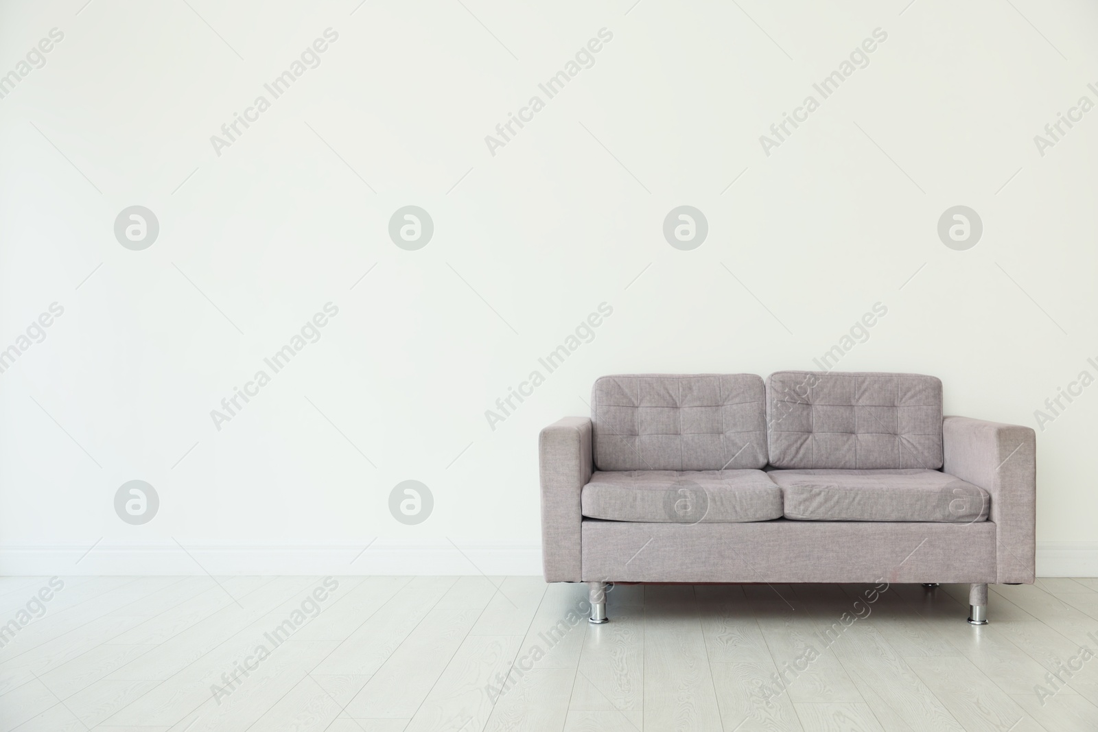Photo of Comfortable gray sofa near white wall in room, space for text