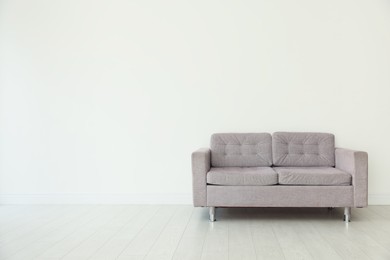 Photo of Comfortable gray sofa near white wall in room, space for text