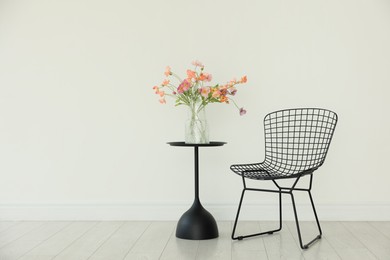 Photo of Stylish metal chair and beautiful flowers in vase on black table indoors, space for text