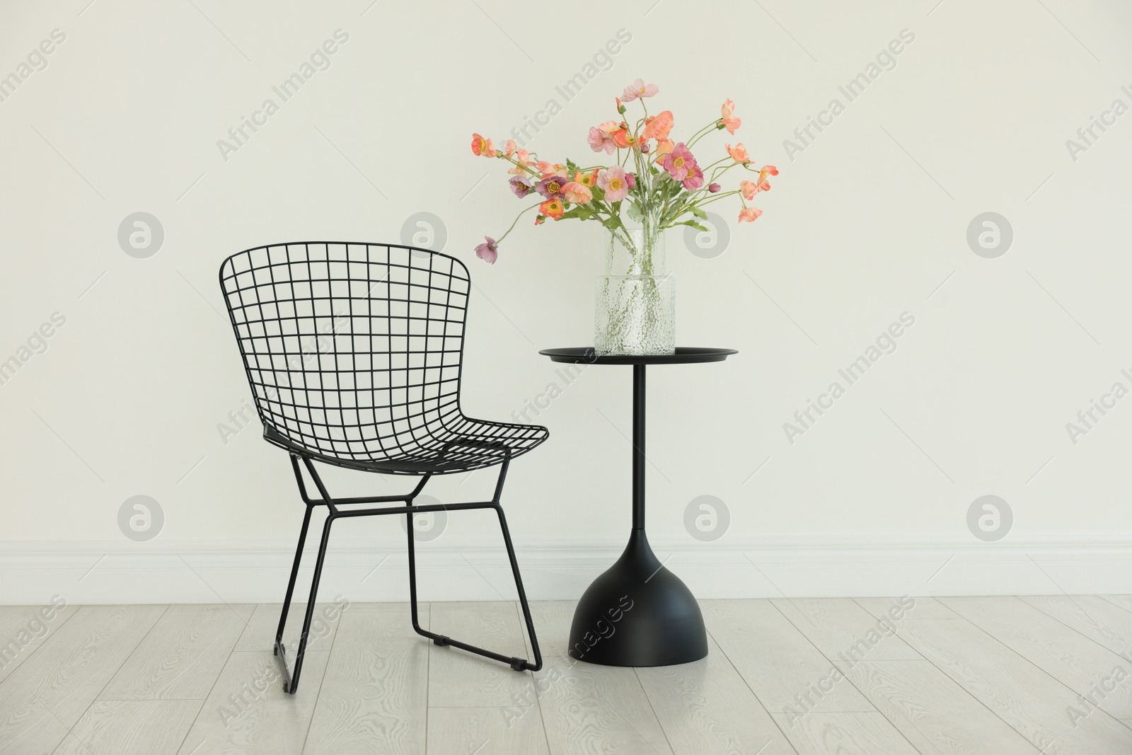 Photo of Stylish metal chair and beautiful flowers in vase on black table indoors. Used stuff
