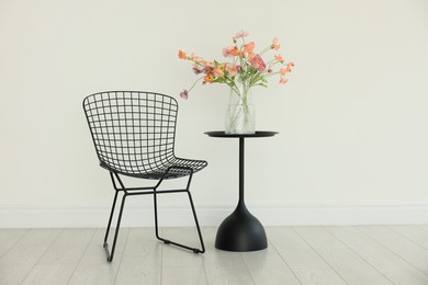 Photo of Stylish metal chair and beautiful flowers in vase on black table indoors. Used stuff