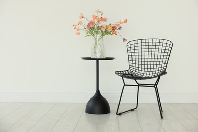 Photo of Stylish metal chair and beautiful flowers in vase on black table indoors, space for text