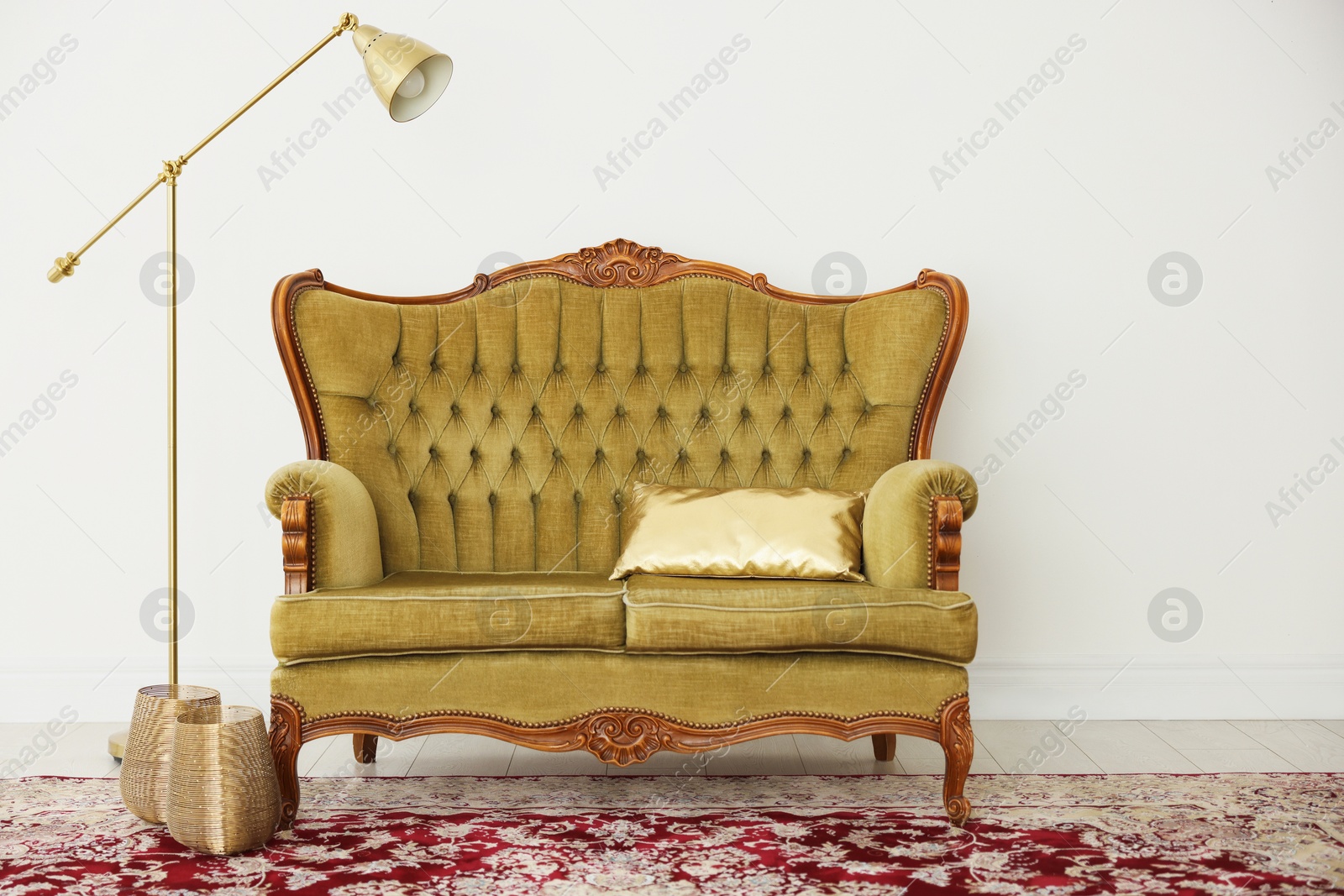 Photo of Stylish sofa with cushion and lamp near white wall indoors. Interior design