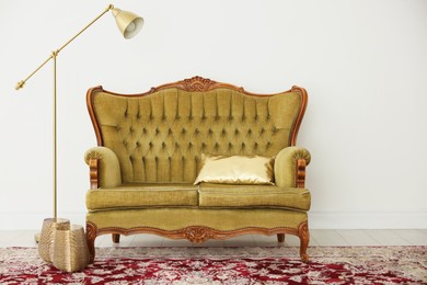 Photo of Stylish sofa with cushion and lamp near white wall indoors. Interior design