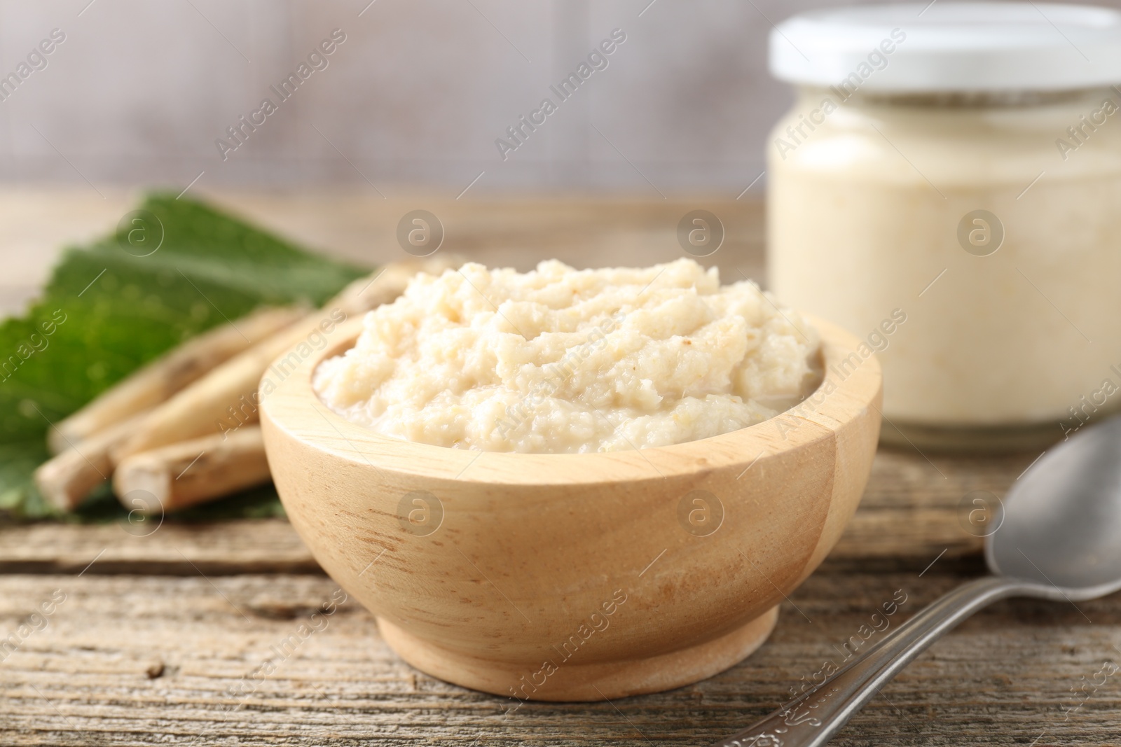 Photo of Tasty horseradish sauce, spoon and roots on wooden table, closeup