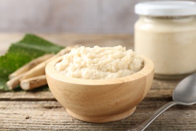 Photo of Tasty horseradish sauce, spoon and roots on wooden table, closeup