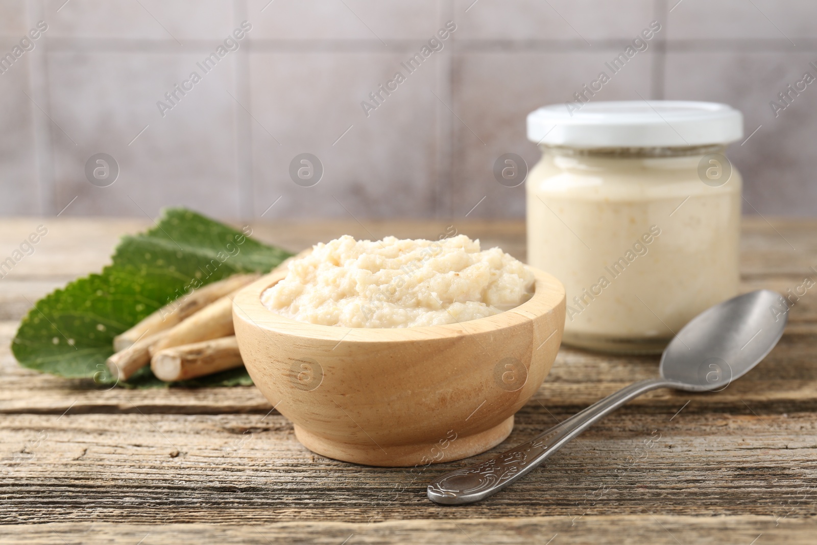 Photo of Tasty horseradish sauce, spoon and roots on wooden table, closeup