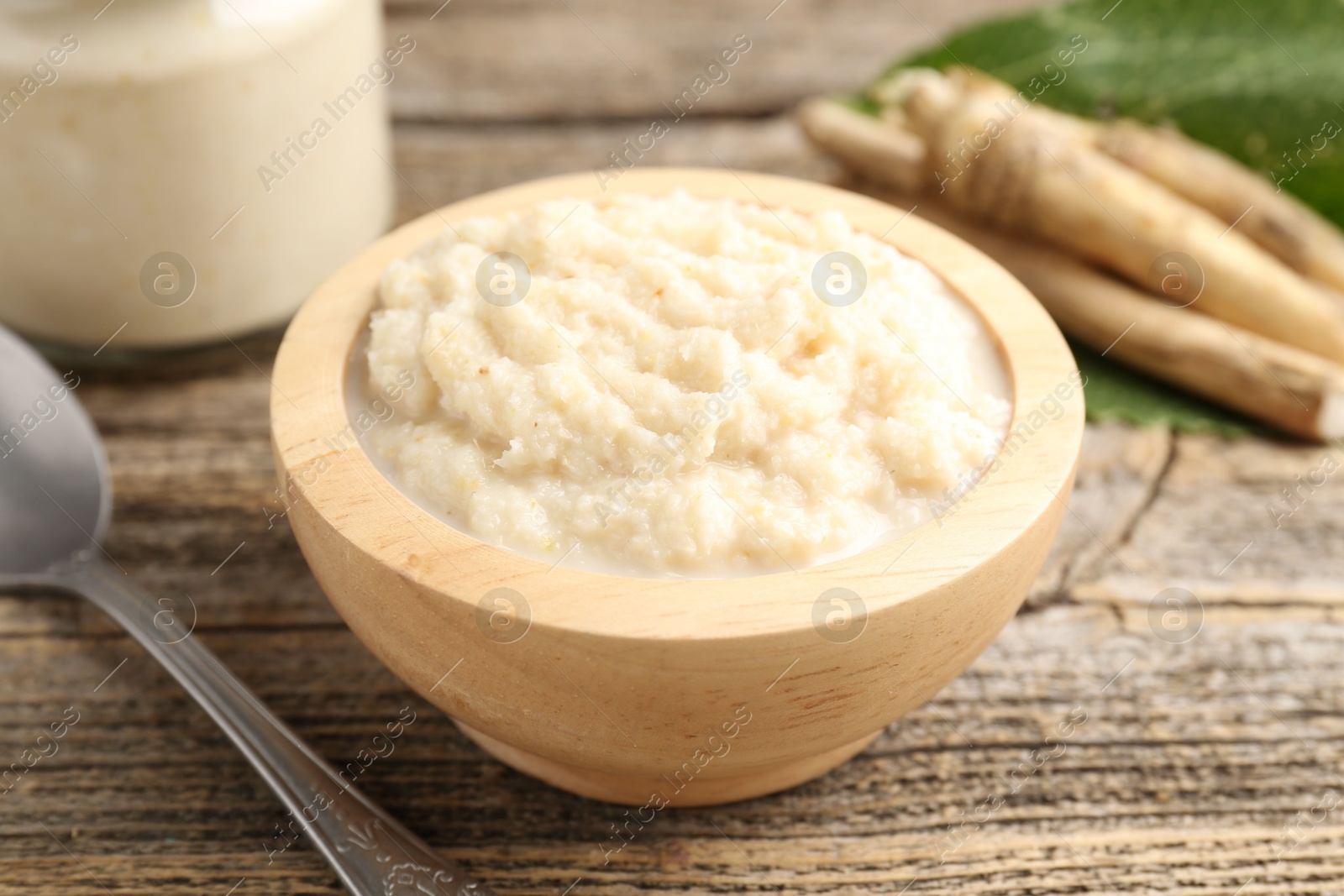 Photo of Tasty horseradish sauce, spoon and roots on wooden table, closeup