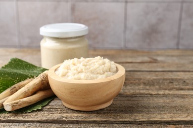 Photo of Tasty horseradish sauce and roots on wooden table. Space for text
