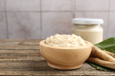 Photo of Tasty horseradish sauce and roots on wooden table. Space for text