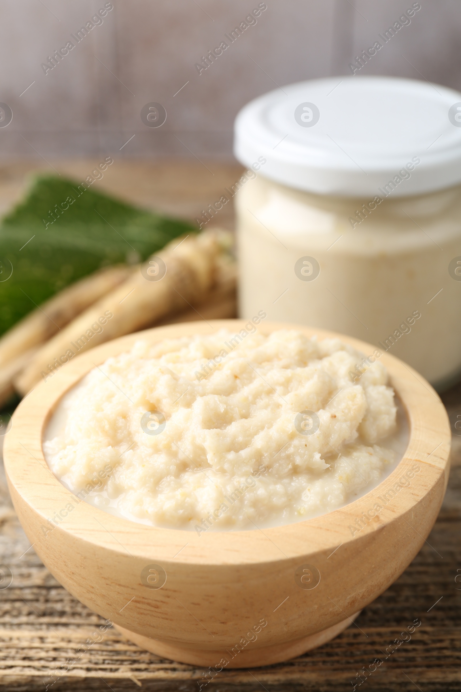 Photo of Tasty horseradish sauce and roots on wooden table, closeup